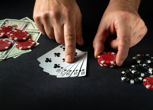 Hráč ukazuje prstem na výherní kombinaci flush v pokeru na černém stole s žetony a penězi v kasinu. - Fotografie, Obrázek