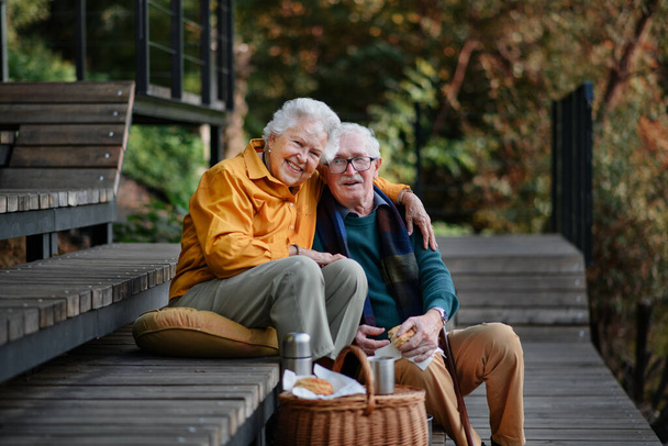 Happy senior couple resting near lake after walk and looking at a smartphone. - 写真・画像