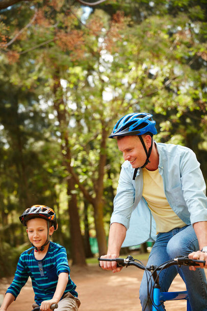 Babamla parka doğru gidiyoruz. Bir baba ve küçük oğlu parktan bisikletle geçiyorlar. - Fotoğraf, Görsel