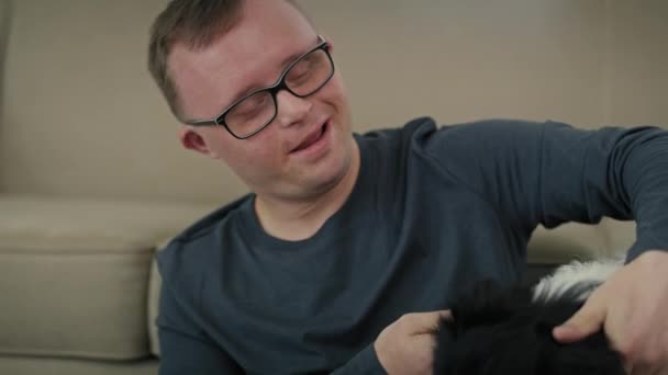 Белый мужчина с синдромом Дауна сидит на полу и играет с собакой. Съемка с красной гелиевой камерой в 8K.      - Кадры, видео