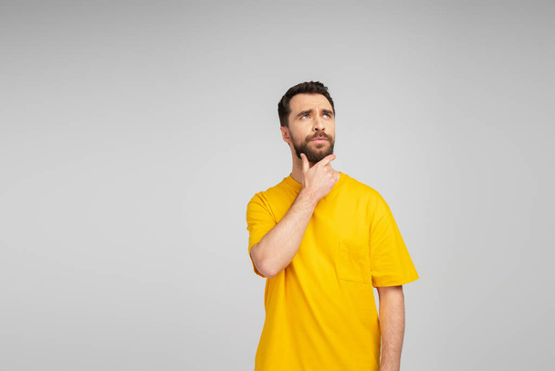 pensive man in yellow t-shirt touching beard and looking away isolated on grey - Foto, Imagem