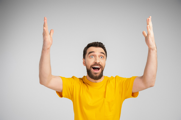 amazed man in yellow t-shirt standing with open mouth and showing wow gesture isolated on grey - Foto, immagini