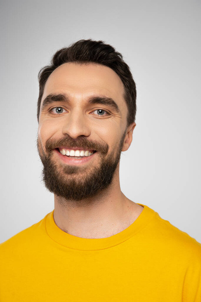 portrait of cheerful brunette man with beard looking at camera isolated on grey - Foto, Bild