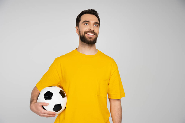 happy bearded football fan holding soccer ball and looking away isolated on grey - Foto, imagen