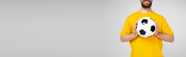Sarı tişörtlü, sakallı ve gülümseyen bir adam futbol topunu gri pankartta tek başına tutuyor. - Fotoğraf, Görsel