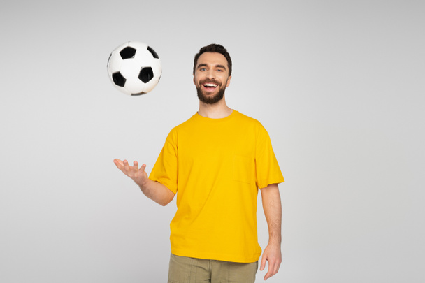 alegre fanático de los deportes en camiseta amarilla jugando con pelota de fútbol aislado en gris - Foto, Imagen