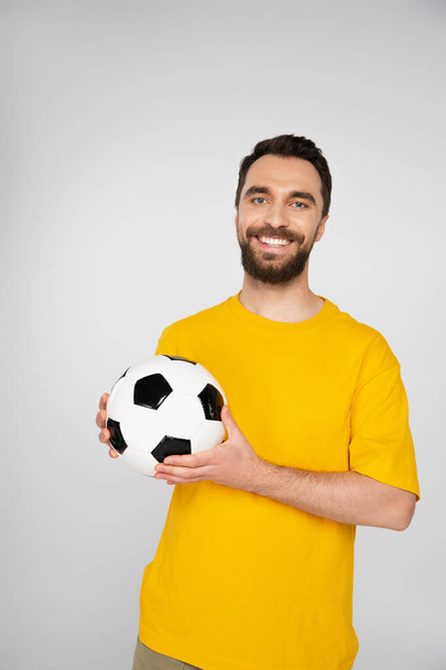 bearded sports fan with soccer ball smiling at camera isolated on grey - Фото, изображение
