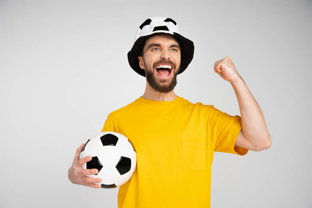 fan de sport excité tenant ballon de football et montrant geste de victoire tout en criant isolé sur gris - Photo, image