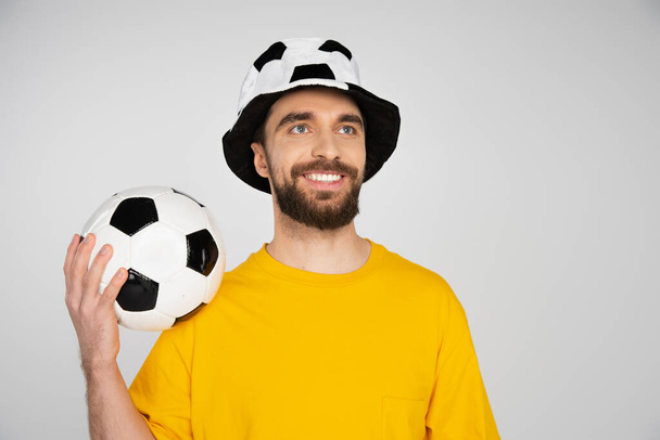 веселый бородатый футбольный болельщик держа футбольный мяч и глядя в сторону изолированы на сером - Фото, изображение
