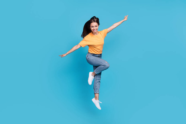 Full length photo of cool shiny lady wear yellow t-shirt jumping high arms sides isolated blue color background. - Foto, immagini