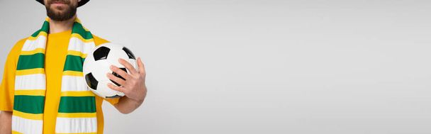 częściowy widok brodatego wentylatora sportowego w szaliku z piłką nożną w paski izolowane na szarości, sztandar - Zdjęcie, obraz