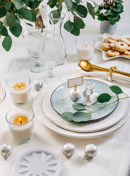 Joulupöydän kattaminen eukalyptuksella, ruokailuvälineillä ja kynttilöillä valkoisella ja vihreällä sävyllä - Valokuva, kuva