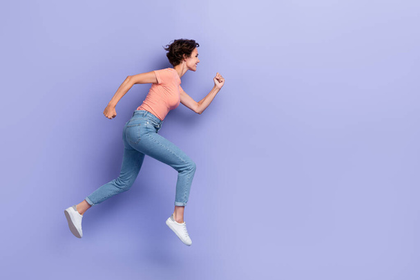 Full length photo of sweet shiny girl dressed orange t-shirt jumping high running fast empty space isolated purple color background. - Valokuva, kuva