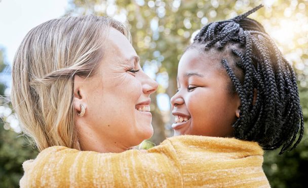 Hug, smile and mother love with girl in a nature park with love, foster care and diversity. Happy, relax and hugging mom and adopted kid bonding together in summer on mothers day or holiday outdoor. - Photo, Image