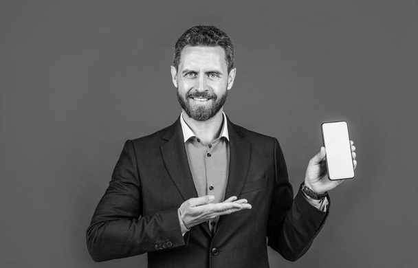mature cheerful man businessman in businesslike suit has grizzled hair presenting product of smartphone, copy space, advert. - Фото, зображення