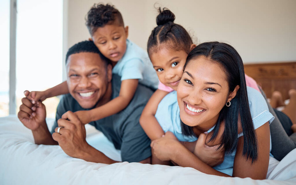 Happy, smile and portrait of a family in a bedroom to relax, play and bond together at their home. Happiness, love and parents relaxing with their children while being playful on a bed at their house. - 写真・画像