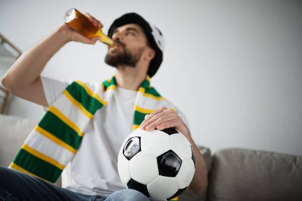 γενειοφόρος άνδρας με καπέλο και μαντήλι κρατώντας το ποδόσφαιρο πίνοντας μπύρα  - Φωτογραφία, εικόνα