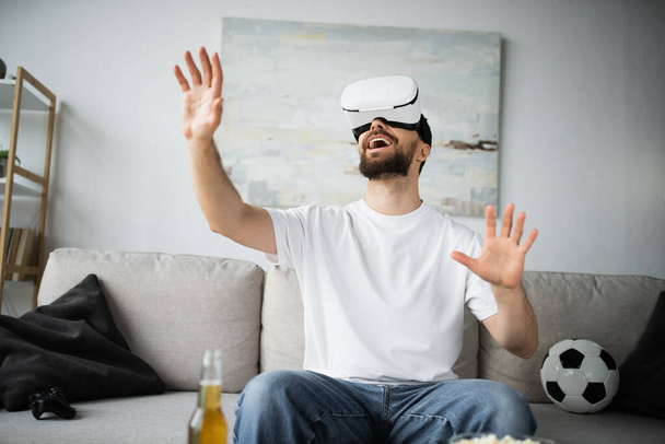 KYIV, UKRAINE - OCTOBER 21, 2022: excited man in vr headset gesturing in living room - Photo, image