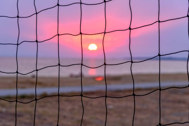 Вид на захід сонця через волейбольну сітку. Драматичний захід сонця над морем
. - Фото, зображення