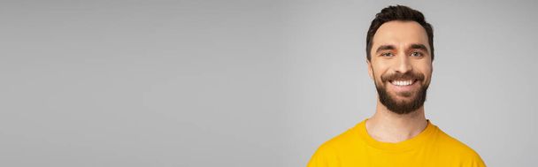 portré vidám szakállas férfi fényes sárga pólóban nézi kamera elszigetelt szürke, transzparens - Fotó, kép