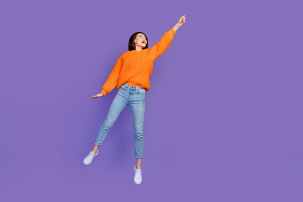 Full size photo of stunning young woman fly hang look empty space dressed stylish orange knitted look isolated on purple color background. - Fotoğraf, Görsel