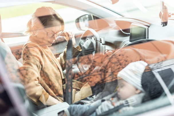 Matka zapínání bezpečnostní pás, řízení rodinné auto, vyřizování pochůzek, zatímco její dítě spí v dětském autosedačce u jejího webu - Fotografie, Obrázek