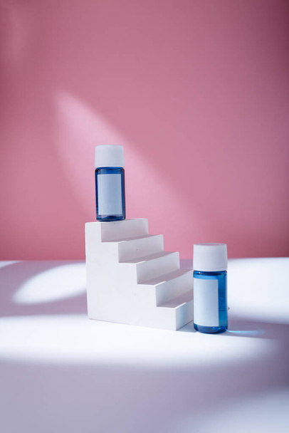 Blue serum or acid mock up bottles with blank label, no brand template on white concrete stairs, pink backdrop. Cosmetics hair glue - Fotó, kép
