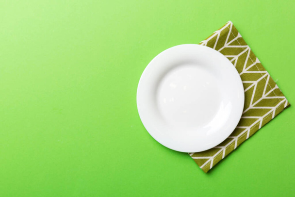 Top view on colored background empty round white plate on tablecloth for food. Empty dish on napkin with space for your design. - Foto, imagen