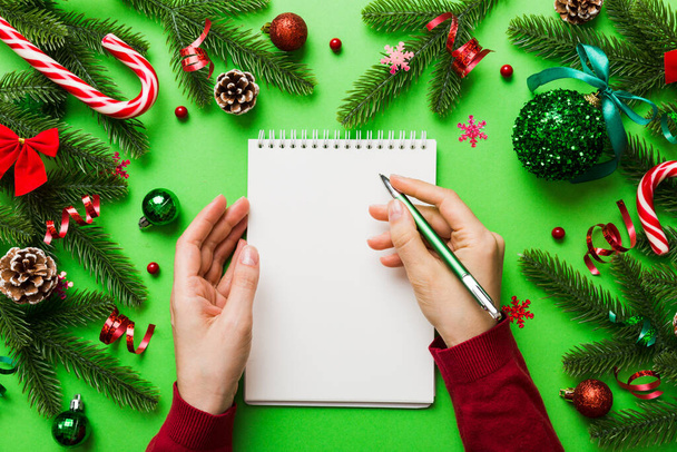 Frau schreibt Weihnachtswunschliste auf Notizbuch auf farbigem Hintergrund mit Weihnachtsdekoration. - Foto, Bild