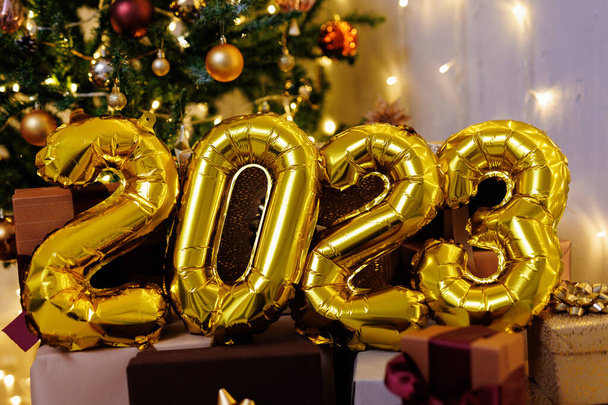 Happy new year concept - golden 2023 air balloon numbers near Christmas tree - Photo, Image