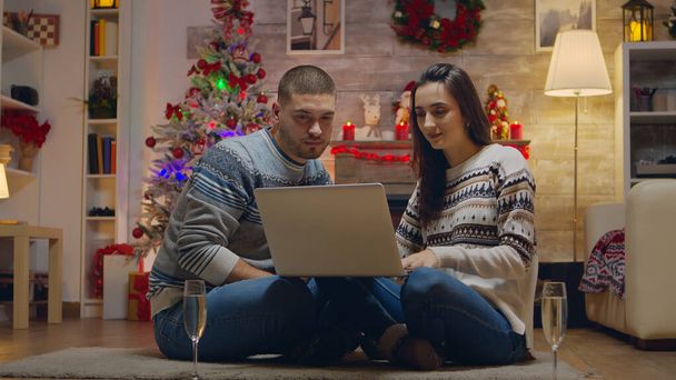 Couple sitting comfortable in front of fireplace doing online shopping for christmas. - Photo, Image