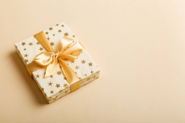 wrapped Christmas or other holiday handmade present in white paper with gold ribbon on colored background. Present box, decoration of gift on colored table, top view with copy space. - Photo, Image
