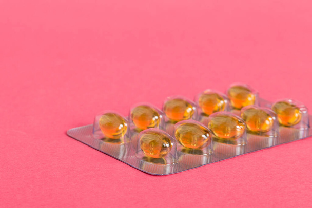 Blister package with fish oil capsules on color background. Medicine pills on a light background. Medicines and prescription pills flat lay background. Yellow medical tablets in blister. - Foto, afbeelding