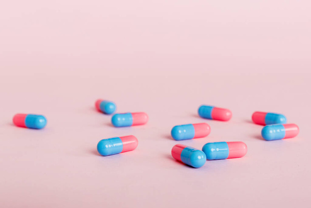 Haufen rosa und blauer Pillen auf farbigem Hintergrund. Tabletten auf einem Tisch verstreut. Haufen roter weicher Gelatinekapsel. Vitamine und Nahrungsergänzungsmittel Konzept. - Foto, Bild