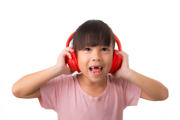 Ευτυχισμένο χαμογελαστό ασιατικό κοριτσάκι ακούγοντας μουσική σε ασύρματα ακουστικά απομονωμένο σε λευκό φόντο. - Φωτογραφία, εικόνα