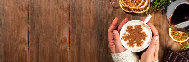 Cappuccino, heißer Schokoladen-Latte-Kaffee mit Schneeflockenmuster auf warmem Holzgrund, Tasse mit heißem Schokoladengetränk in Frauenhand, Kopierraum von oben. Weihnachten Winter gemütliche Café Banner Hintergrund - Foto, Bild