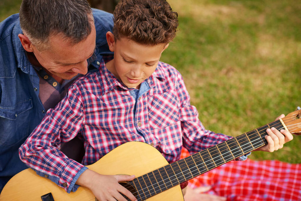 Piszę melodię z tatą. ojciec uczy syna grać na gitarze siedząc na zewnątrz - Zdjęcie, obraz