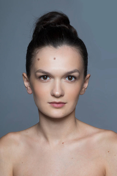 Vorderseite Nahaufnahme Porträt einer schönen brünetten jungen Frau mit natürlichem Make-up und engen Haaren, isoliert grauen Hintergrund. - Foto, Bild