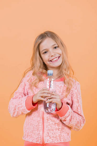 Happy child with drinking water. Girl smile with water bottle on orange background. Drink healthy water. Life source concept. Nutrition, healthcare, lifestyle, punchy pastel. - Fotografie, Obrázek