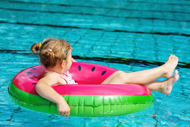 Счастливая маленькая девочка, играющая с цветным надувным кольцом в открытом бассейне в солнечный летний день. Дошкольник учится плавать. Активный отдых летом. - Фото, изображение