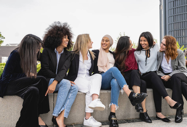 Egy csapat boldog multiracionális nő, akik öltönyben ülnek, és egymásra néznek. - Fotó, kép