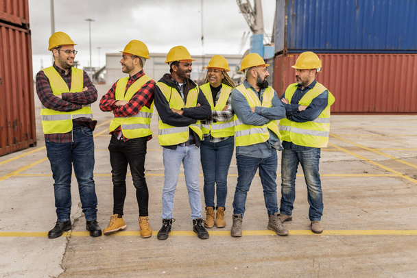 Groep multiraciale arbeiders met armen gekruist in reflecterende vesten en helmen die naar elkaar kijken - Foto, afbeelding