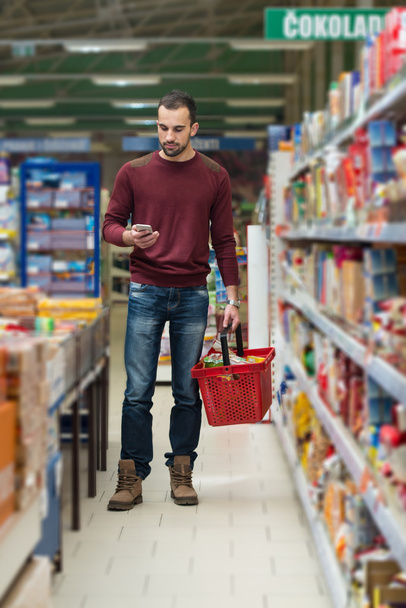 Jonge Man te typen op mobiele telefoon in supermarkt - Foto, afbeelding