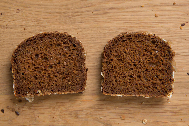 Два ломтика ржаного коричневого хлеба с семенами льна и подсолнечника лежат бок о бок на разделочной доске, плоская укладка - Фото, изображение