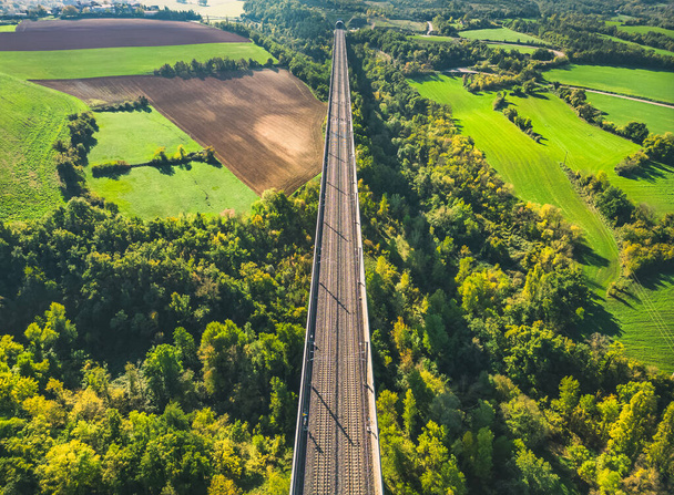 Aerial view of the railroad tracks for high-speed trains on the flyover. Panoramic autumn view of the surrounding fields and forests and the surrounding mountains. - Φωτογραφία, εικόνα