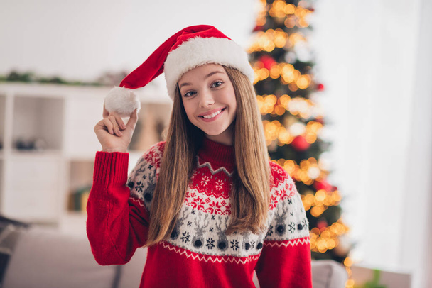 Photo of funky cheerful girl toothy smile hand hold touch festive headwear pompom christmastime house indoors. - Foto, Imagen