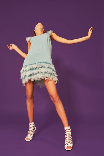 Photo of pretty young blonde girl in blue cocktail dress dancing on purple background in studio. Indoor portrait of caucasian young lady expressing her emotions - Photo, Image