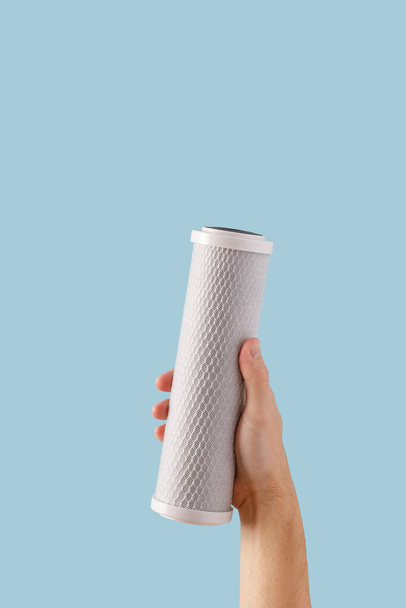hand water filter. cartridge with a carbon filter of household drinking water purification systems in hands on a blue background - Fotoğraf, Görsel