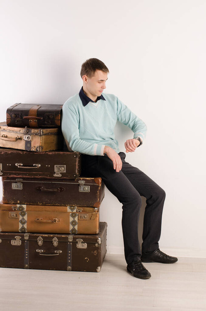Молодой человек опирается на стопку чемоданов, смотрит на часы, на свет - Фото, изображение
