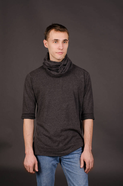 Portrait of a young man in a black sweater and jeans, on a studio gray background - 写真・画像